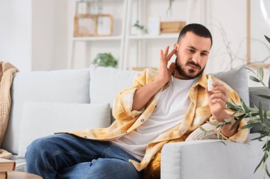 Kulak damlalı genç adam evdeki kanepede oturuyor.