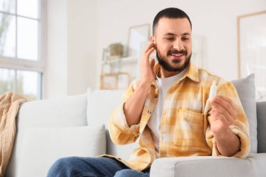Kulak damlalı genç adam evdeki kanepede oturuyor.