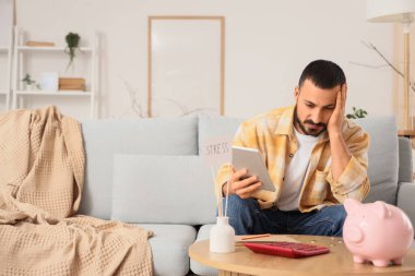 Evde para sayan tabletli stresli bir genç adam.