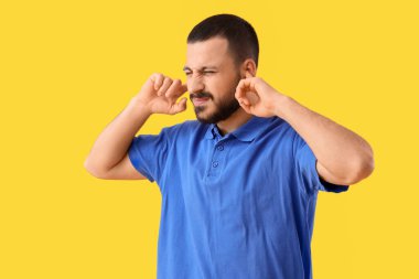 Sarı arka planda kulaklarını kapatmakta zorlanan genç bir adam.