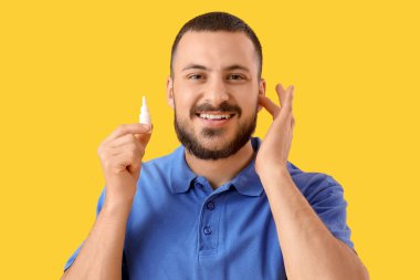 Sarı arka planda kulak damlası olan genç adam, yakın plan.