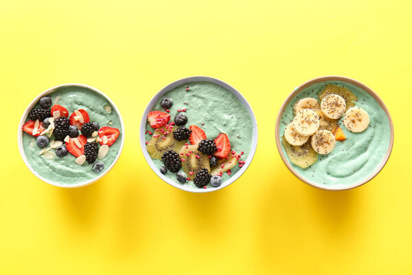 Bowls with tasty spirulina smoothie, fruits and berries on yellow background