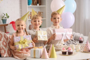 Küçük şirin çocuklar parti şapkalarında keklerle ve hediye kutularıyla evde doğum günü kutluyorlar.