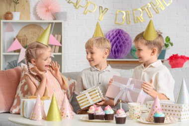 Küçük şirin çocuklar parti şapkalarında keklerle ve hediye kutularıyla evde doğum günü kutluyorlar.