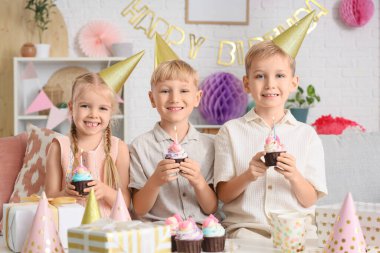 Küçük şirin çocuklar parti şapkalarında keklerle ve hediye kutularıyla evde doğum günü kutluyorlar.