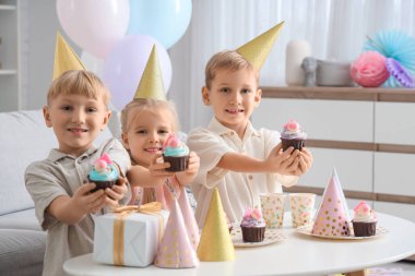 Evde kek ve hediye kutusuyla parti şapkası takmış şirin küçük çocuklar.