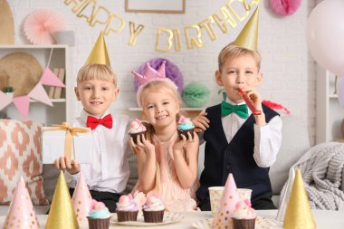 Evde kek ve hediye kutusuyla parti şapkası takmış şirin küçük çocuklar.