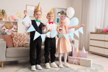 Parti şapkası takmış şirin küçük çocuklar. Kek, hediye kutuları ve evde doğum gününü kutlayan çelenkler.