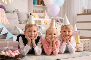 Küçük şirin çocuklar parti şapkalarında keklerle ve hediye kutularıyla evde doğum günü kutluyorlar.