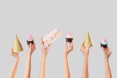 Doğum günü kekleri, hediye kutuları ve gri arka planda parti şapkaları olan birçok kadın eli.