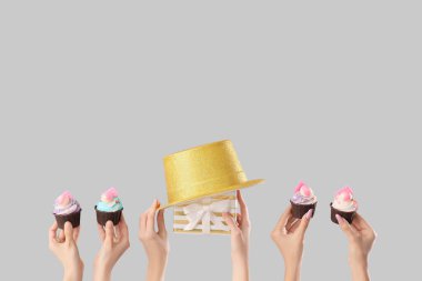 Doğum günü pastaları, parti şapkası ve gri arka planda hediye kutusu olan bir sürü kadın eli.