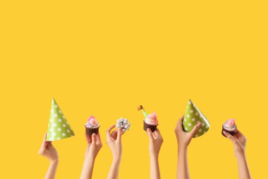 Bir sürü kadın eli ve doğum günü kekleri, ıslık ve sarı arka planda parti şapkaları.