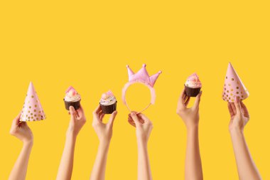 Doğum günü kekleri, parti şapkaları ve sarı arka planda taçla bir sürü kadın eli