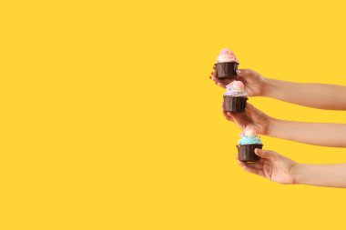 Sarı arka planda doğum günü kekleri olan bir sürü kadın eli.