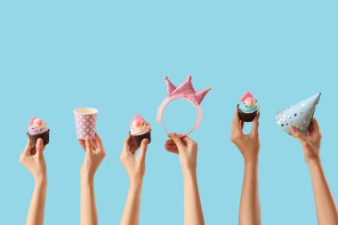 Doğum günü kekleri, parti aksesuarları ve mavi arka planda tek kullanımlık fincanları olan bir sürü kadın eli.