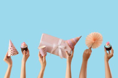 Doğum günü kekleri, parti şapkaları ve mavi arka planda hediye kutusu olan bir sürü kadın eli.