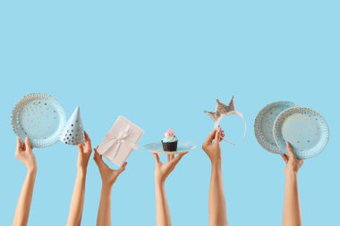 Doğum günü pastası, tek kullanımlık tabaklar ve mavi arka planda hediye kutusu olan bir sürü kadın eli.