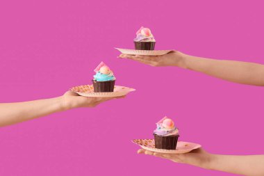 Birçok kadın eli, mor arka planda doğum günü pastaları olan tabakları tutuyor.