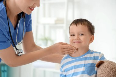 Klinikte küçük şirin bir çocuğun boynunu muayene eden kadın bir çocuk doktoru.