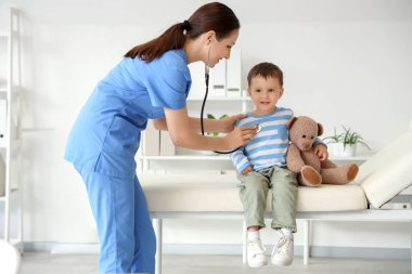 Steteskoplu kadın çocuk doktoru. Klinikte küçük şirin bir çocuğu dinliyor.