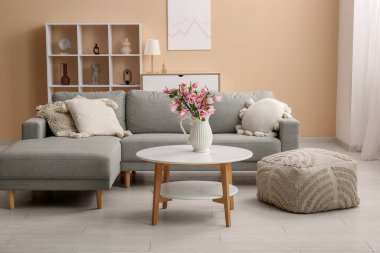 Üzerinde güzel manolya çiçekleri olan vazo şık oturma odasındaki gri kanepenin yanında.