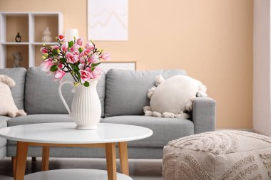 Üzerinde güzel manolya çiçekleri olan vazo şık oturma odasındaki gri kanepenin yanında.