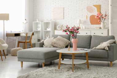 Güzel manolya çiçekleri ve dergilerle dolu vazo modern oturma odasındaki gri kanepenin yanında.