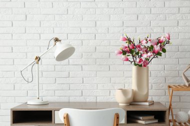 Güzel manolya çiçekleri olan vazo, şık bir odada beyaz tuğla duvarın yanında iş yerinde.