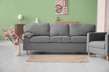 Modaya uygun oturma odasında gri kanepenin yanında güzel manolya çiçekleri olan vazo.