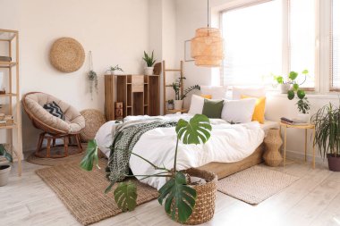 Yeşil bitkilerle, koltuk ve raf üniteleriyle aydınlık yatak odasının içinde.