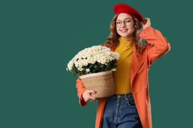 Yeşil arka planda güzel kasımpatı çiçekleri olan şık bir genç kadın.