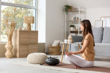 Aroma sopalarıyla evde meditasyon yapan genç bir kadın.