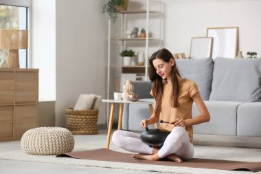 Meditasyon yapan genç bir kadın evde glukofon çalıyor.