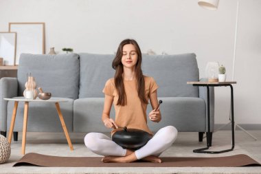 Meditasyon yapan genç bir kadın evde glukofon çalıyor.