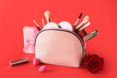 Makyaj malzemeleriyle dolu kozmetik çanta, kırmızı arka planda güzel bir gül ve hediye kutusu. Sevgililer Günü kutlaması