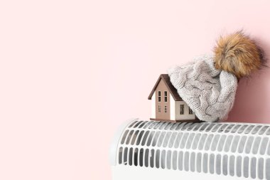 Pembe arka planda, ısıtıcı takılı sıcak şapkalı ev modeli. Isıtma kaydetme kavramı