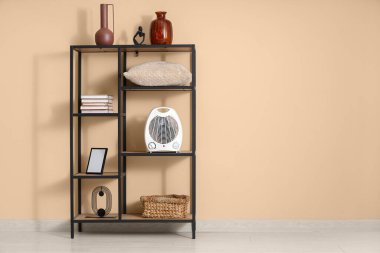 Raflarda modern elektrikli vantilatör ısıtıcısı ve bej duvarın yanında dekor var.