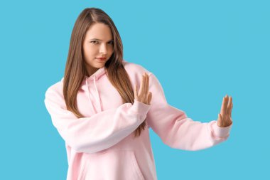 Güzel, genç, çatık kaşlı bir kadın mavi arka planda bir şeyi reddediyor.