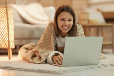 Sıcak ekoseli genç bir kadın akşam evde dizüstü bilgisayar kullanıyor.