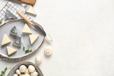 Açık arkaplanda lezzetli işlenmiş peynir, bıçak ve mantar üçgenleri olan bir tabak.