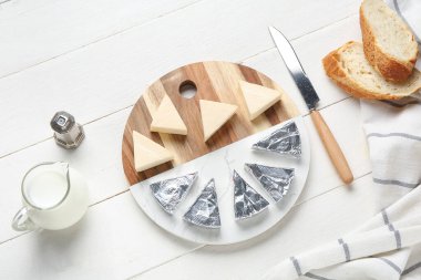 Hafif ahşap zemin üzerinde lezzetli işlenmiş peynir, ekmek, süt ve bıçak üçgenleri ile kompozisyon