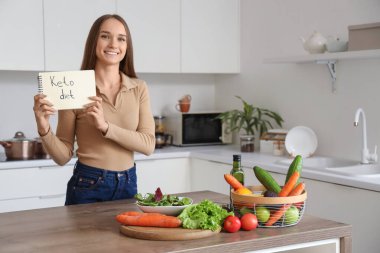 Elinde KETO diyeti ve mutfakta yemek olan not defteri tutan genç bir kadın.