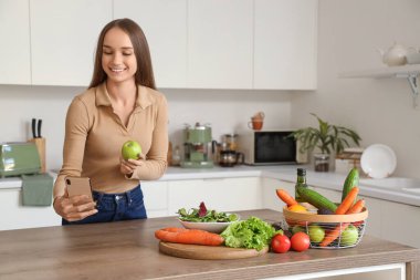 Mutfakta cep telefonu kullanan elmalı genç bir kadın. Keto diyet kavramı