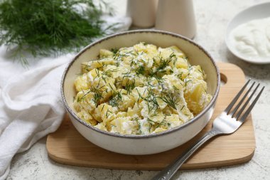 Bir kase lezzetli patates salatası, dereotlu, ekşi kremalı ve çatallı hafif grunge arkaplanlı.