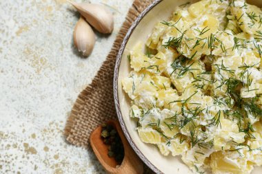 Bir kase lezzetli patates salatası, dereotlu, biberli ve beyaz grunge arka planda sarımsaklı.