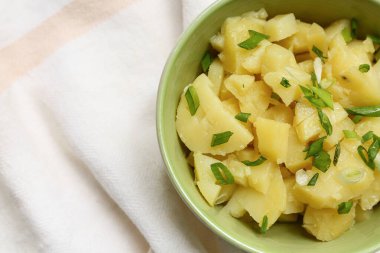 Bir kase lezzetli patates salatası ve yeşil soğanlı peçete.