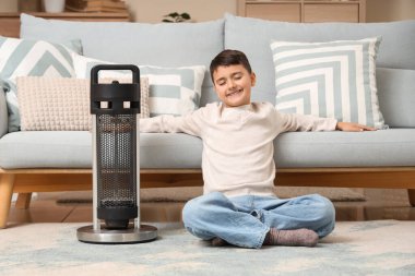 Evdeki halının üzerinde elektrikli ısıtıcısı olan sevimli çocuk.