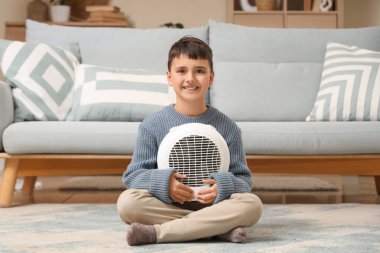 Evdeki halının üzerinde elektrikli fan ısıtıcısı olan sevimli çocuk.