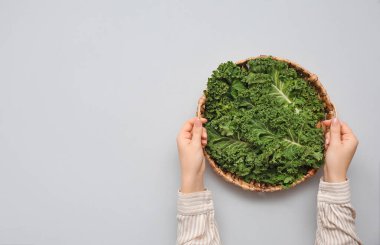 Gri arka planda taze lahana yapraklarıyla hasır tepsisi olan kadın elleri