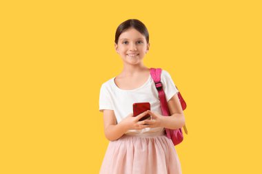 Sırt çantalı genç kız sarı arka planda cep telefonu kullanıyor.